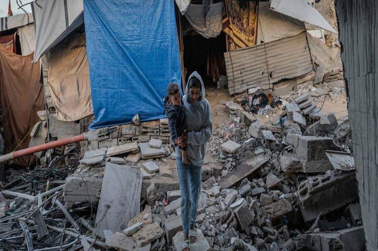 شابة فلسطينية تحمل طفلها الرضيع وسط أنقاض منزلها المدمر في مدينة غزة